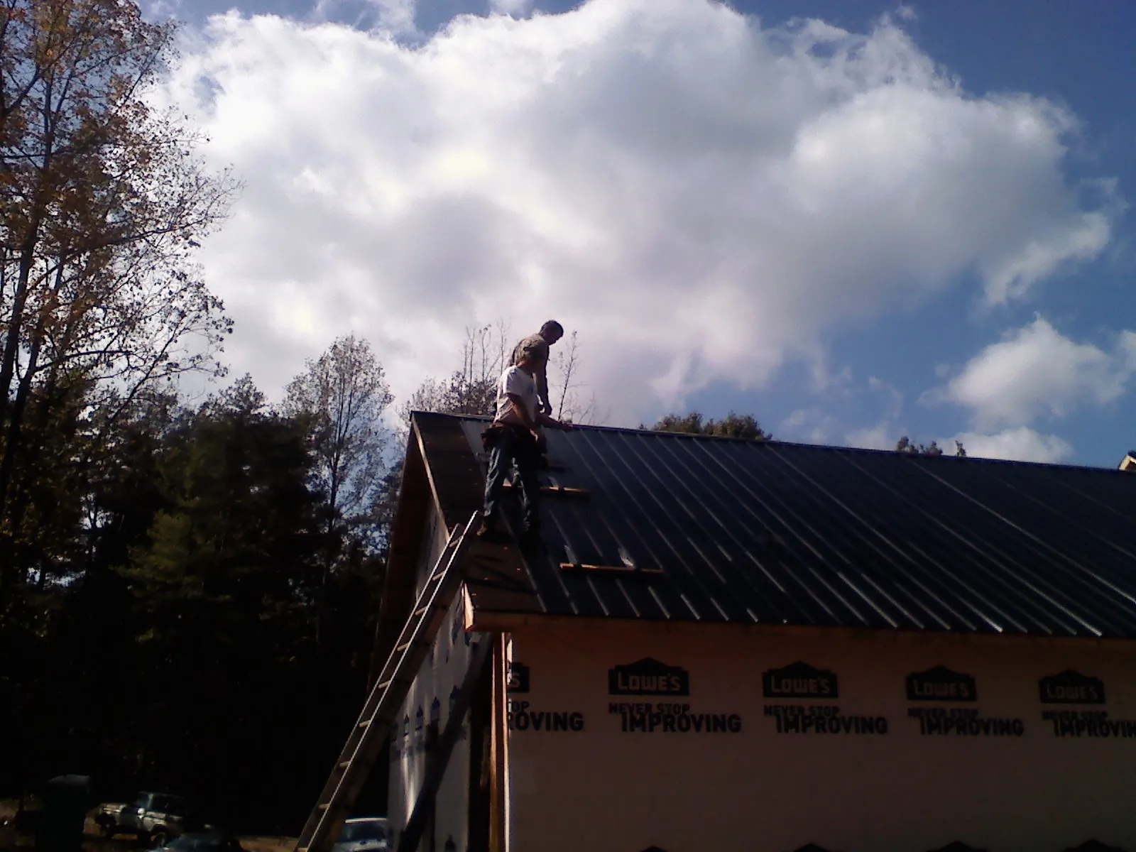 Roofer fastening dark metal panels high against a cloudy sky, from a Roof Inspection job in Lakeland